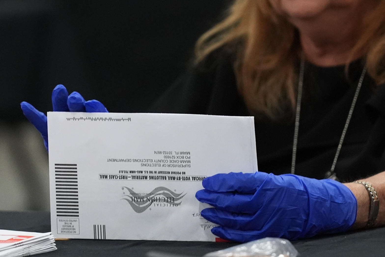 Election worker in blue gloves holding a vote-by-mail envelope